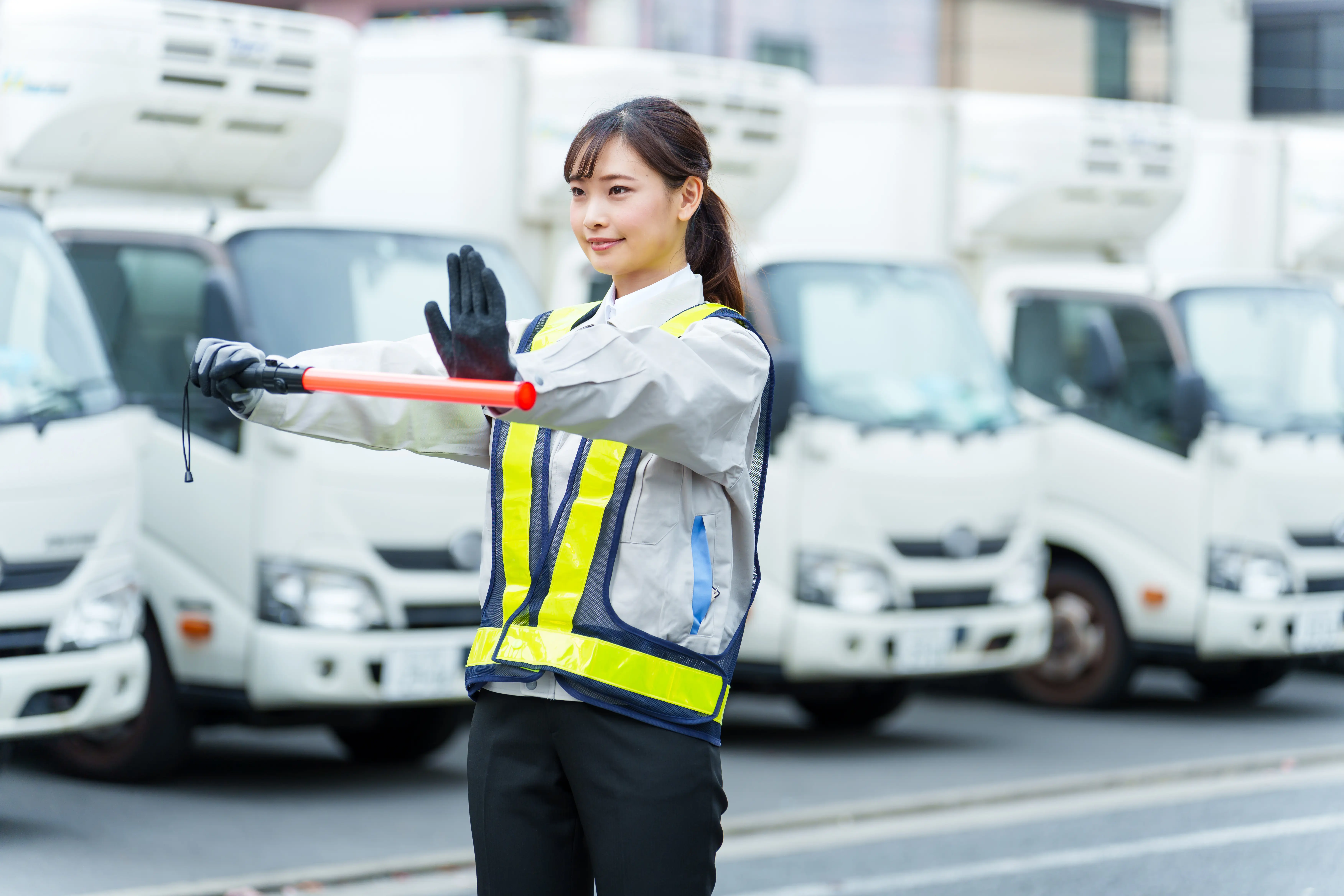 警備員が安全ベストを着用し、誘導灯を使って車両を案内する様子